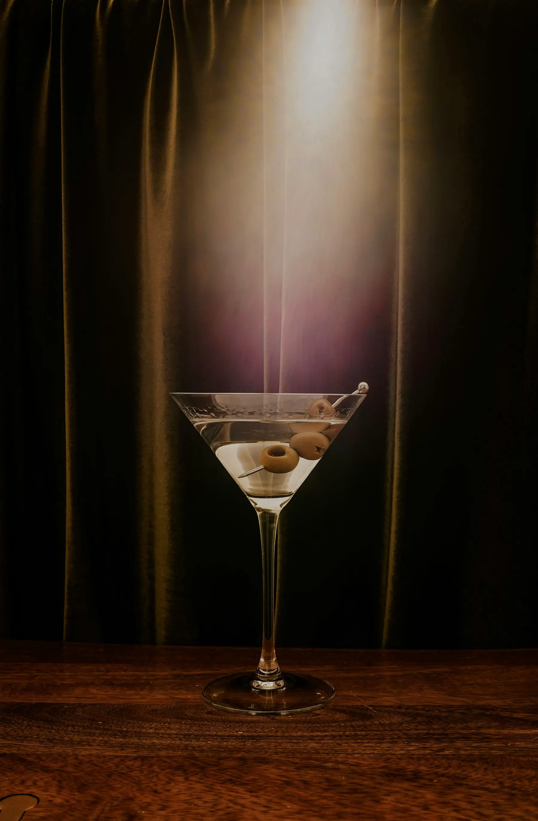 Martini seco con aceitunas bajo un foco, sobre una barra de madera